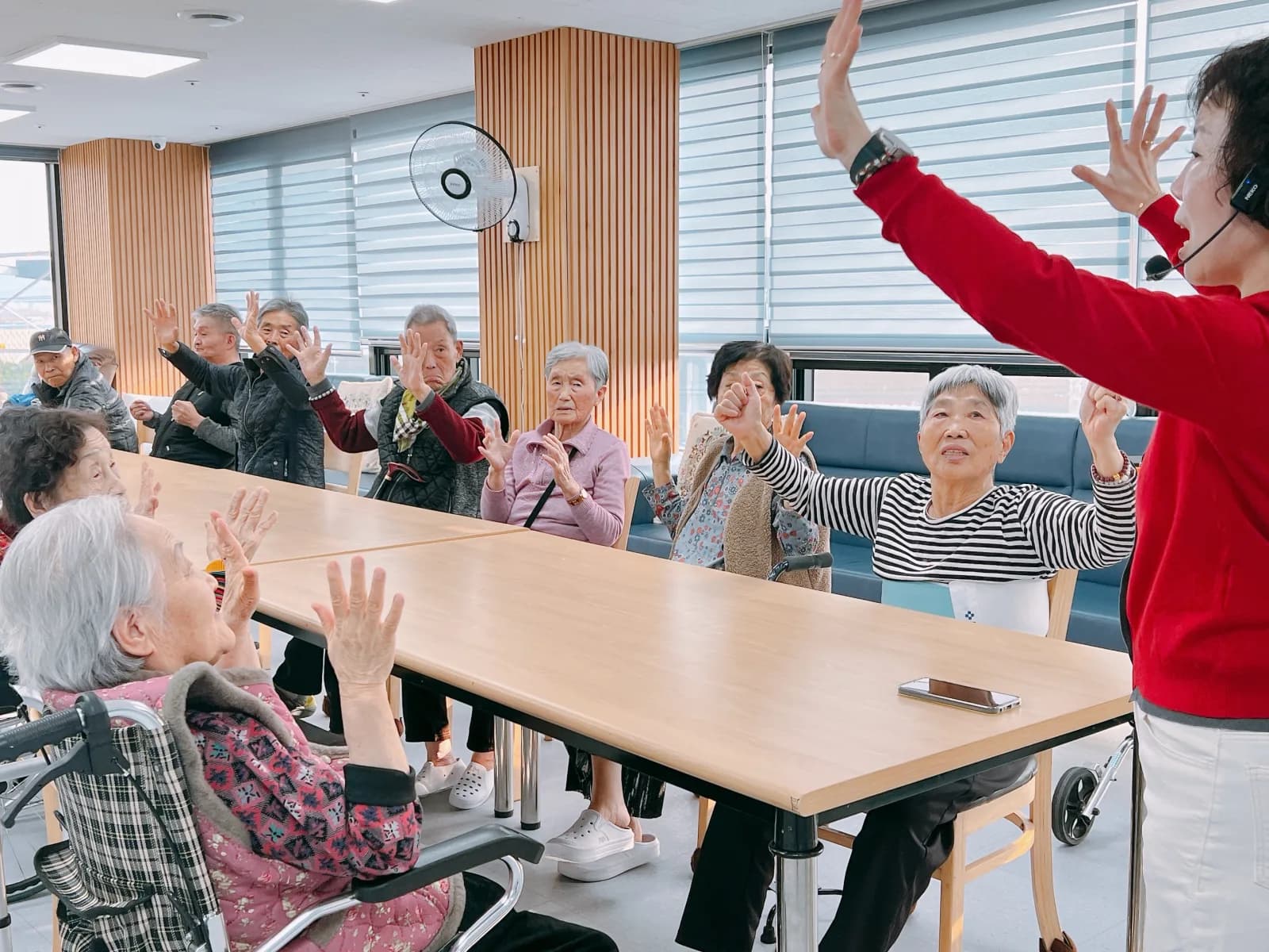 경기우리요양원 어르신들이 강사와 함께 팔을 들어 올리며 체조하는 모습